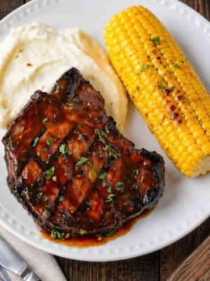 A close up of grilled hoisin pork chops served with mashed potatoes and corn on the cob.