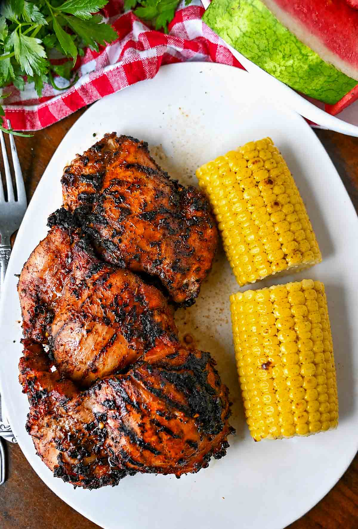 Grilled chicken thighs on a platter with corn on the cob.