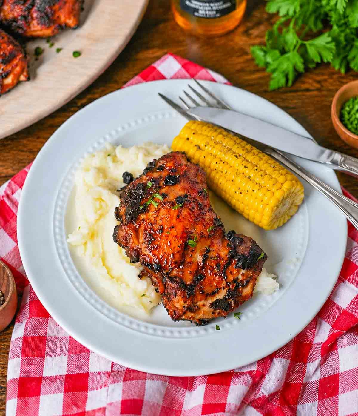 Grilled chicken thigh with mashed potatoes and corn on the cob on a plate.