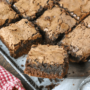 A close up of a slice gooey chocolate butter cake being lifted from a baking pan.
