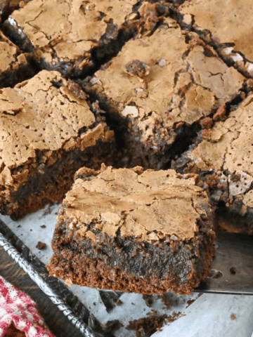A close up of a slice gooey chocolate butter cake being lifted from a baking pan.