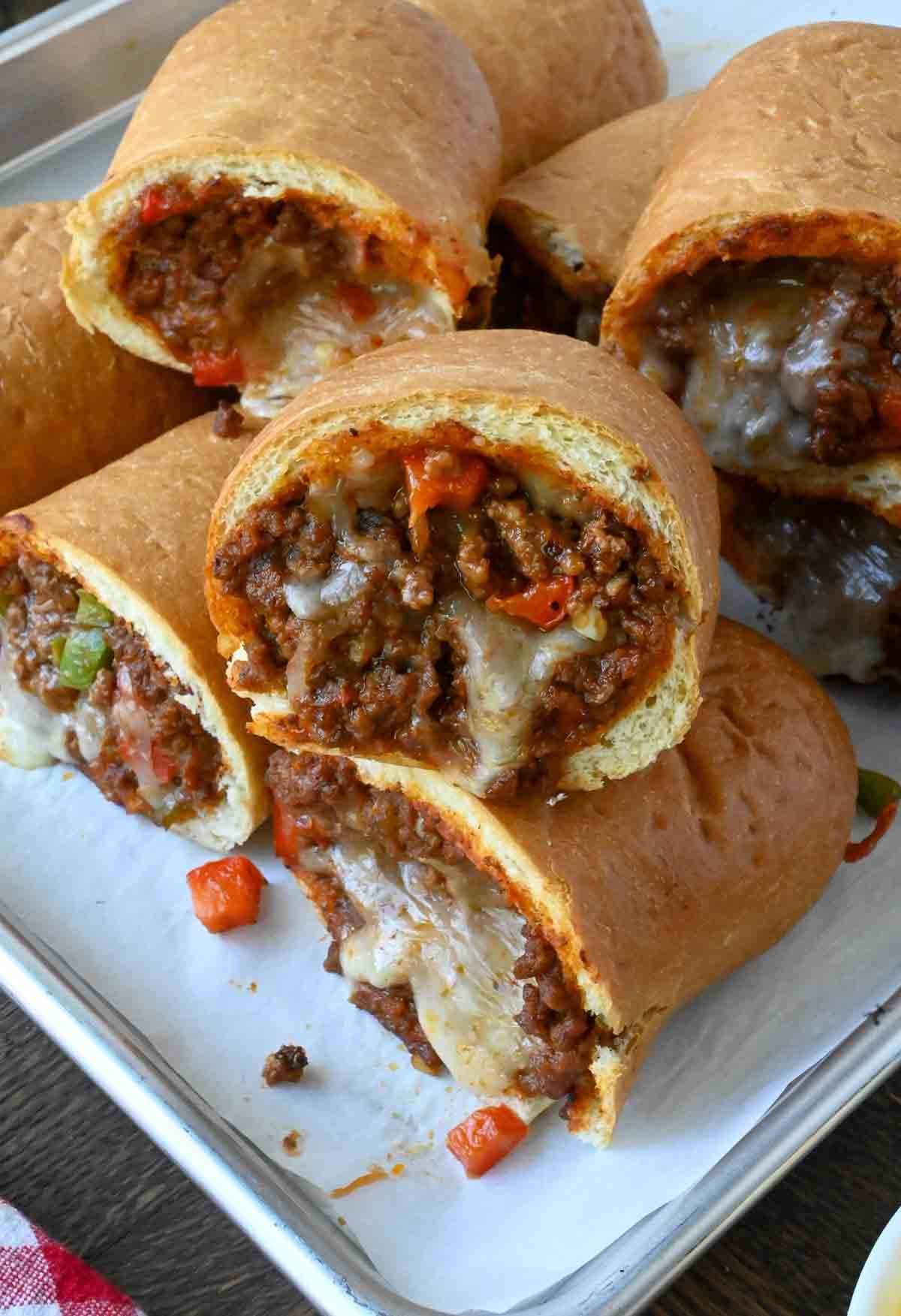A baking sheet with stuffed sloppy joe rolls stacked on each other.