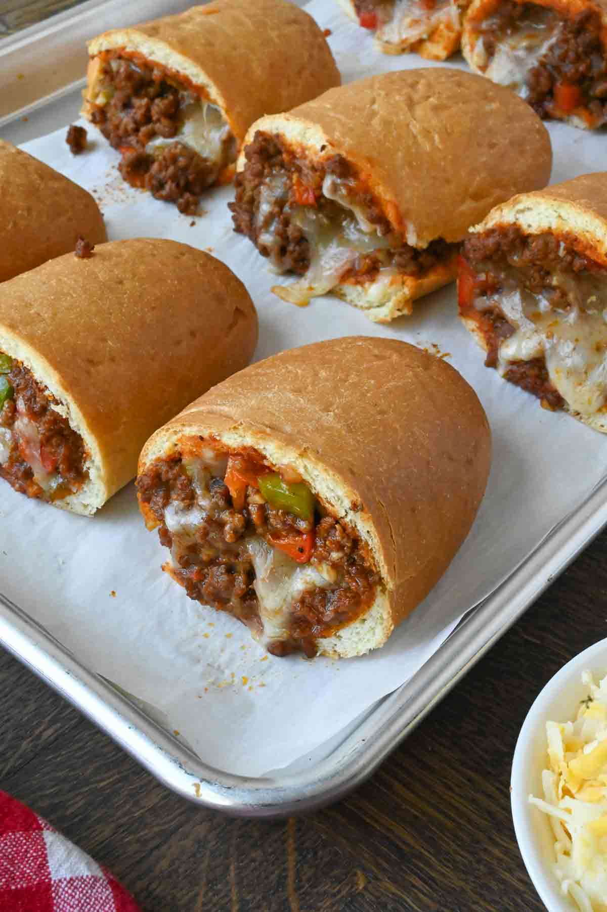 Sloppy joe stuffed rolls on a parchment lined baking sheet.