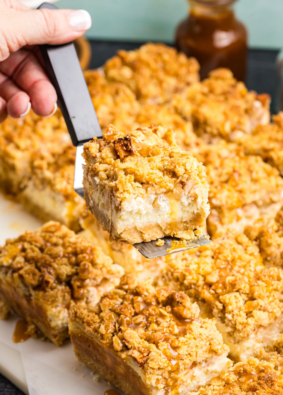 A spatula removing a bite of this apple cheesecake bar.