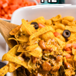 A wooden spoon scooping out some frito pie from a dish.