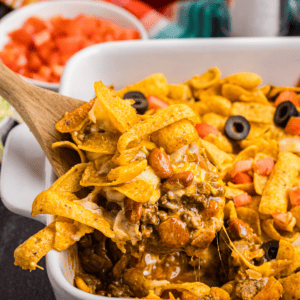 A wooden spoon scooping out some frito pie from a dish.
