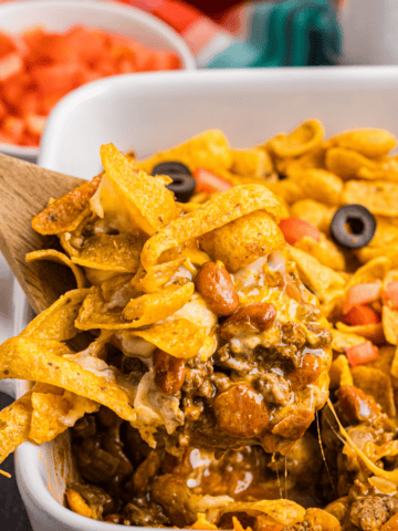A wooden spoon scooping out some frito pie from a dish.