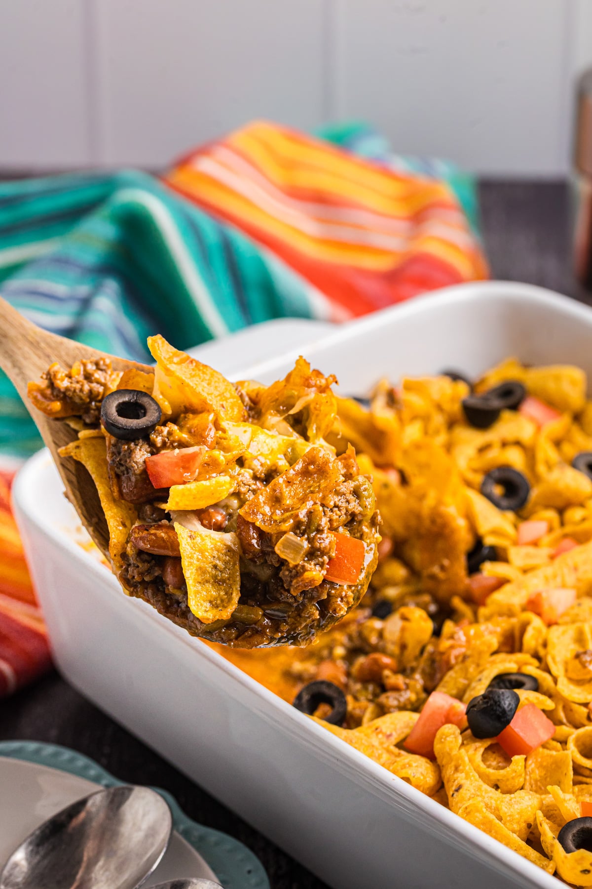 A wooden spoon scooping out some frito pie for the casserole dish.