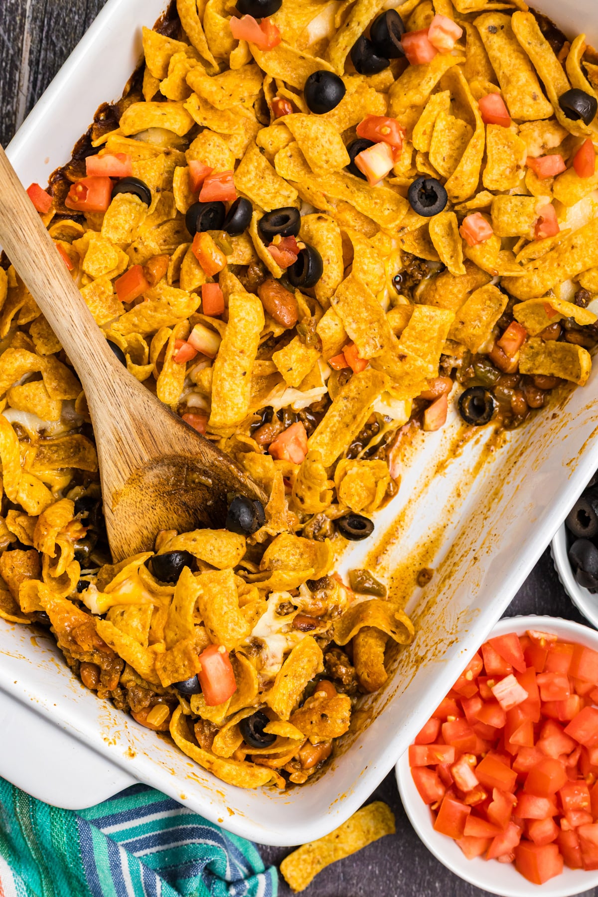 Frito pie in a casserole dish with a wooden spoon.